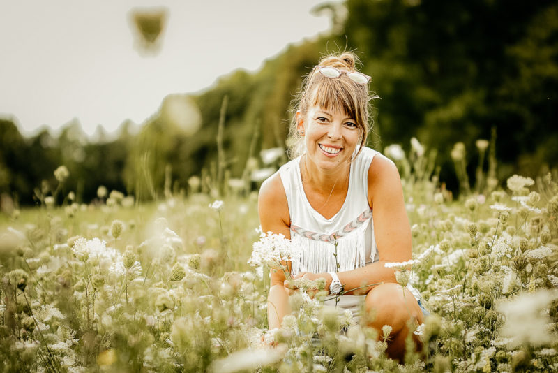 Frau sitzt in einer Blumenwiese.