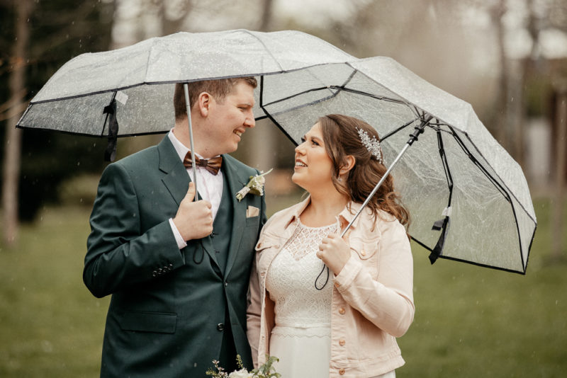 Hochzeitspaar unter zwei Regenschirmen.
